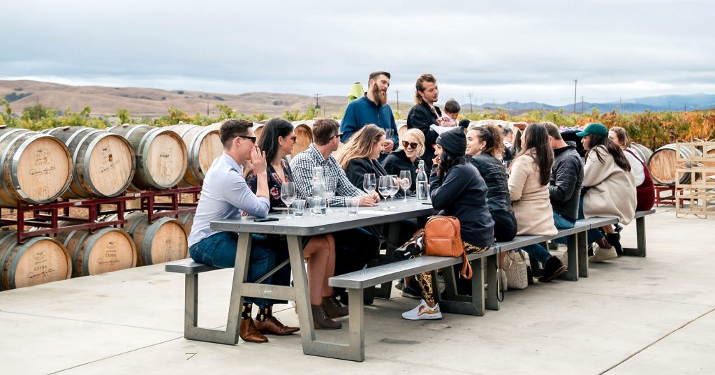 A group of friends and family gathered at a long table above the vineyard at Darcie Kent Estate Vineyard