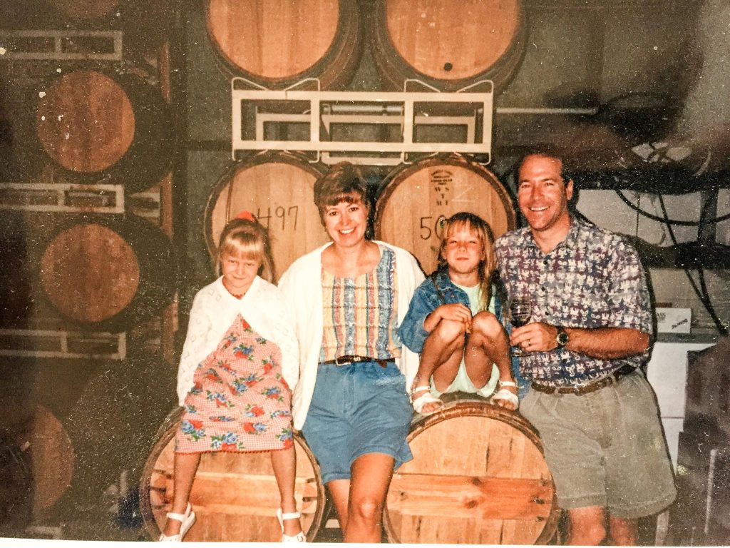 Darcie Kent, husband David, and daughters Kailyn and Amanda posing in front of and sitting on wine barrels